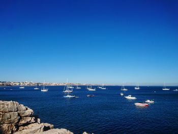 Boats sailing in sea against clear blue sky