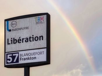 Low angle view of road sign against rainbow in sky