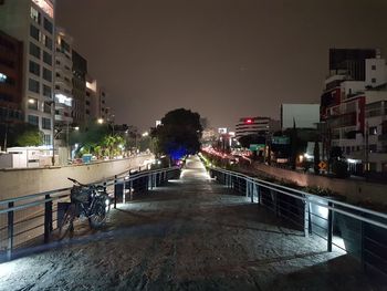 Illuminated street amidst buildings against sky at night