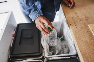 Hands of woman recycling plastic bottles in kitchen at home