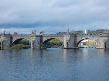 Arch bridge over river against cloudy sky
