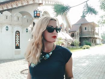 Young woman wearing sunglasses standing against building