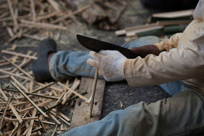 Low section of man cutting wood on field