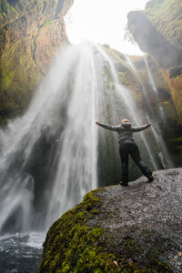 Low angle view of woman looking at waterfall while standing on rock