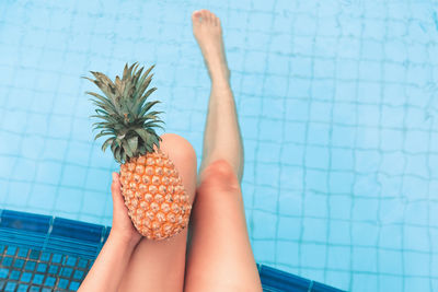 Low section of woman holding pineapple while sitting at poolside