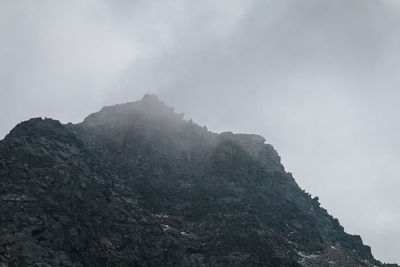 Low angle view of mountain in foggy weather against sky