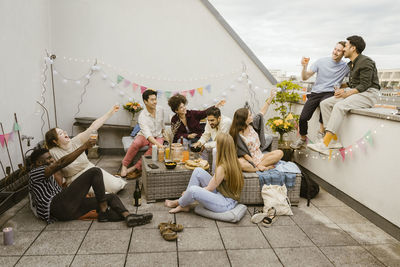 Male and female multiracial friends celebrating with drinks while sitting at rooftop deck