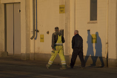 Full length of men standing against yellow wall