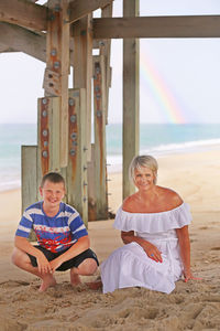 Portrait of mother and son crouching under pier on beach