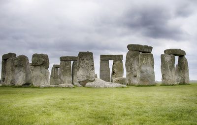 Stone structure in field against cloudy sky