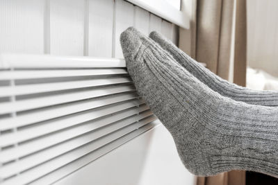 Legs in knitted socks warming over electric heater freezing for cold. girl warms feet on radiator