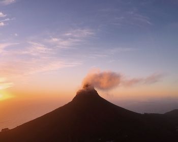 Smoke emitting from volcanic mountain against sky during sunset