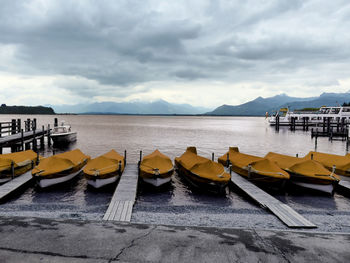 Rowboats moored in river against cloudy sky