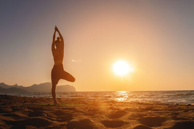 Full length of woman standing at beach against sky during sunset