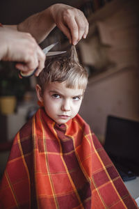 Middle aged father cutting hair to his son by himself at home looking video broadcast on laptop