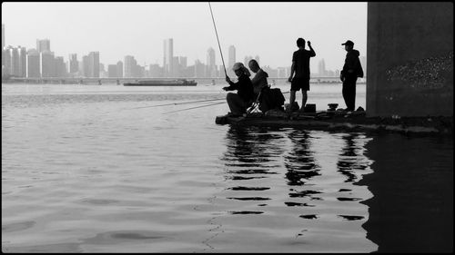 People on sea by cityscape against sky