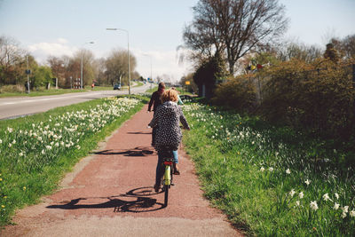 Rear view of woman riding bicycle on road against sky