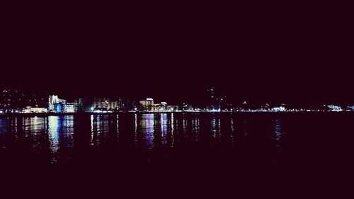 Illuminated buildings by river against sky at night