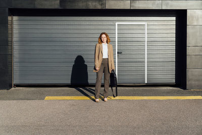 Businesswoman with laptop bag in front of corrugated wall