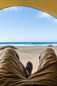 Low section of man at beach against sky