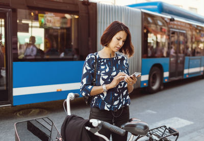 Young woman using mobile phone while sitting on street