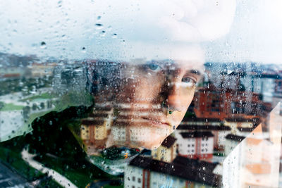 Close-up portrait of woman seen through wet glass window
