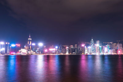 Illuminated city by river against sky at night