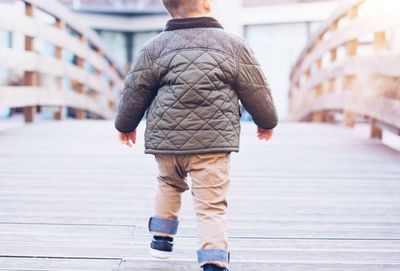 Rear view of boy walking on footbridge in city