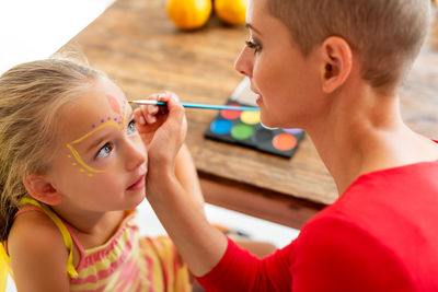 Close-up of mother applying face paint on daughters face at home