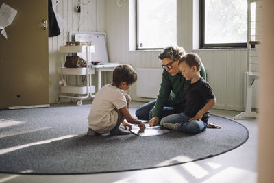 Preschool kids studying with senior female teacher while sitting on carpet in classroom at school