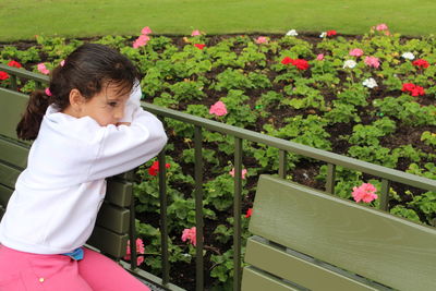 Child girl sad or thinking looking to flowers in a garden