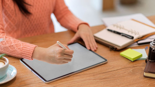 Midsection of woman using mobile phone while sitting on table