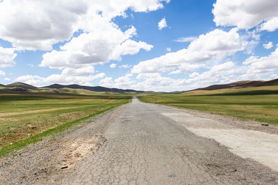 Empty road amidst field against sky