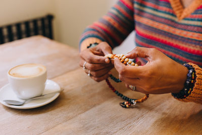 Female hands holding mala beads at a table with a cinnamon roll and a coffee cup