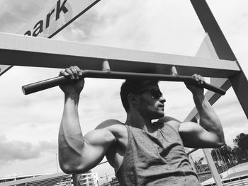 Young man exercising on metal railing against sky