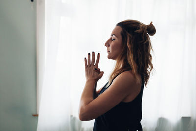 Side view of woman looking through window at home