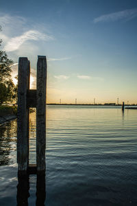 Wooden pole/pier over river against sky during sunset