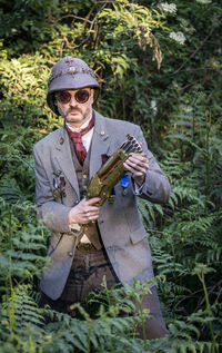 Portrait of man in sunglasses holding handgun against tree