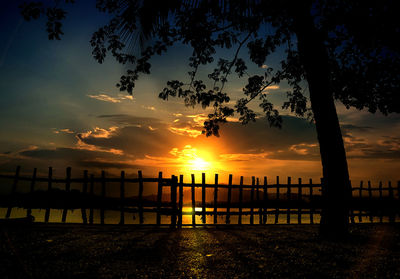 Silhouette wooden posts on beach against sky during sunset