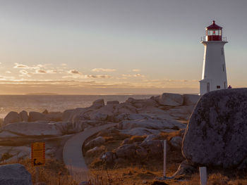 Lighthouse by sea and buildings against sky