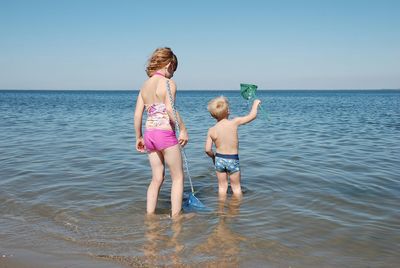 Full length rear view of children on sea against clear sky