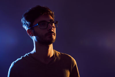 Close-up of thoughtful young man wearing eyeglasses against purple background