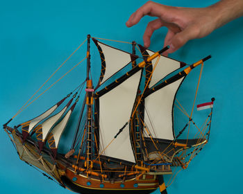 Low angle view of person holding sailboat against blue sky