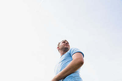 Low angle view of young man looking up against clear sky