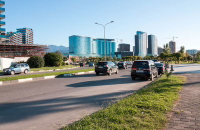 Cars on road by buildings in city against clear sky