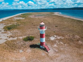 Lighthouse on beach by sea against sky