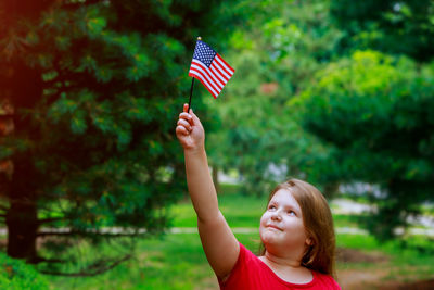 Cute overweight girl with small american flag standing at public park