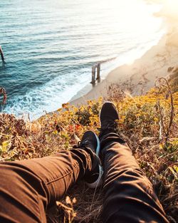 Low section of man relaxing at beach during sunset