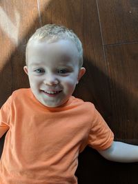 Portrait of cute smiling boy lying on hardwood floor at home