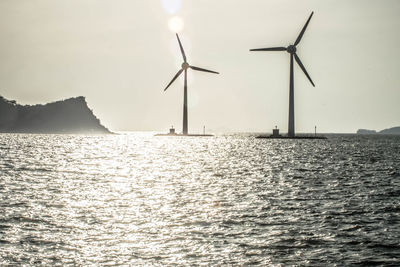 Windmills by sea against sky during sunset